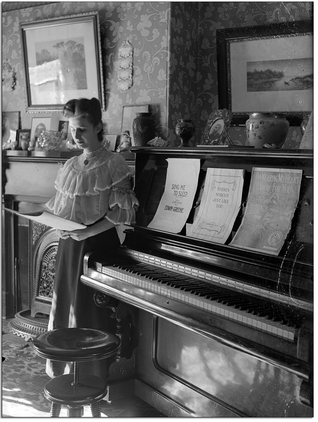 Unidentified woman looking at sheet music, posed beside a piano, [between 1898 and 1920]
