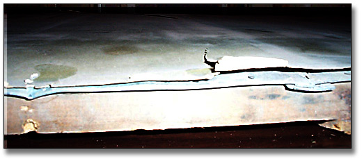 Photographie : Une vue en coupe montrant le haut de l’épreuve sur gélatine-argent, soulevée et déchirée du bord du dos protecteur en métal.