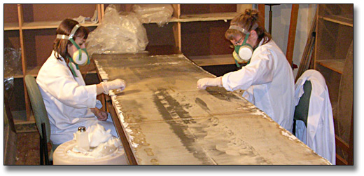 Photo: Two conservators work across the table from each other removing varnish from one of the winter panorama