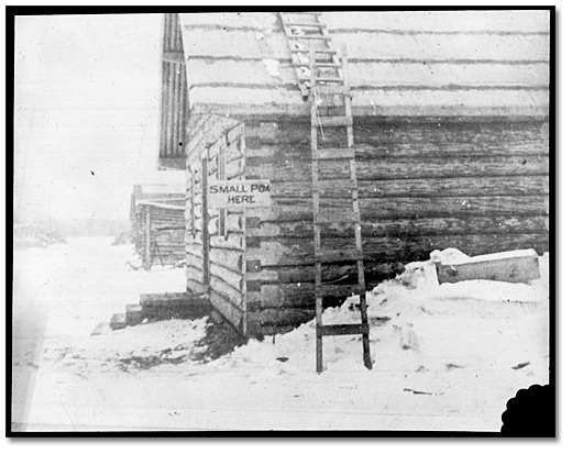 Photo: A log building at a work camp, with a “Smallpox here” sign affixed to it, [between 1900 and 1920]