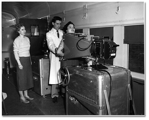 Photographie : Femmes subissant un test de dépistage de la tuberculose à la clinique ambulante de radiographie pulmonaire établie dans un train par l’Association ontarienne de prévention de la tuberculose, Ontario, [vers 1950]