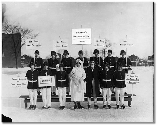 Photographie : Patineurs en costume d’apparat et tenant des affiches annonçant la Semaine de la santé à Sarnia. Janvier 1925