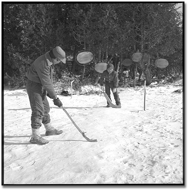 Photo: Boys from Moose Factory playing hockey in a winter camp. Beaver pelts hanging in background, 1959