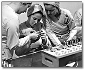 Black and white photograph of women in work tunics and hats working in an industrial setting during World War Two