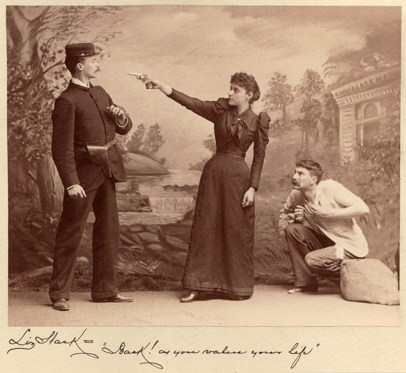 Three white actors. A woman points a gun at a man in uniform and a man crouches behind her. The woman’s lines are below.