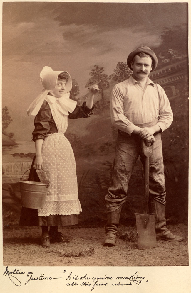 Two white actors playing farmers. A woman holds a bucket and points at a man with a shovel. The woman’s lines are below.