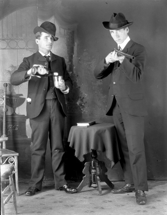 Two white male actors performing with a gun and a bottle of alcohol.
