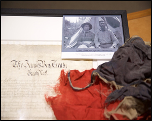 Photo de Stan Wesley mettant en vedette le document écrit du Traité de la baie James (Traité no 9), une photo du chef Michel Batise et de sa femme à la cérémonie de signature du traité à Fort Matachewan en 1906, et un drapeau provenant de la cérémonie.