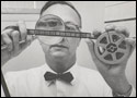 Photo of a man looking at a microfilm reel with a magnifying glass