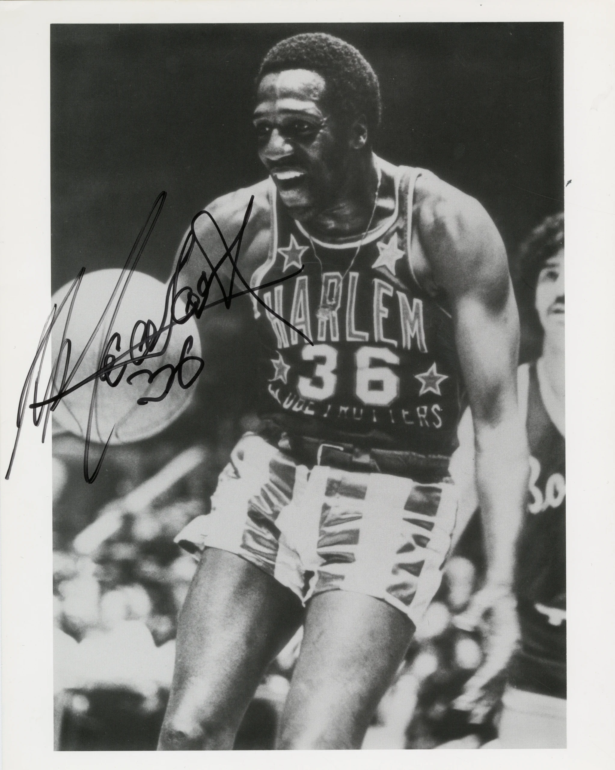 Photo noir et blanc d’un joueur de basketball noir en tenue d’équipe, tenant un ballon, prise en plein match. La photo comporte une grande signature manuscrite à l’encre noire.
