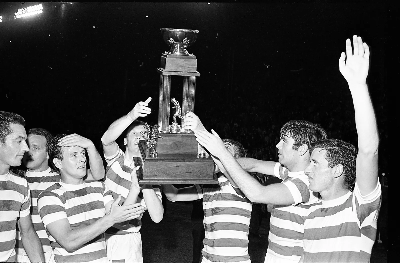 Black-and-white photo of players from Celtic FC in uniform lifting the CNE exhibition trophy.