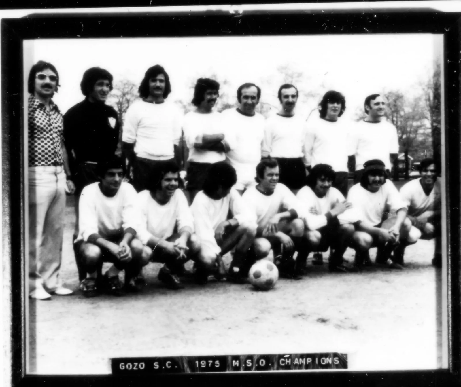 Black-and-white team photo of the Gozo soccer club taken outdoors in their white jerseys, with the coach on the left side of the image and a soccer ball in the centre.