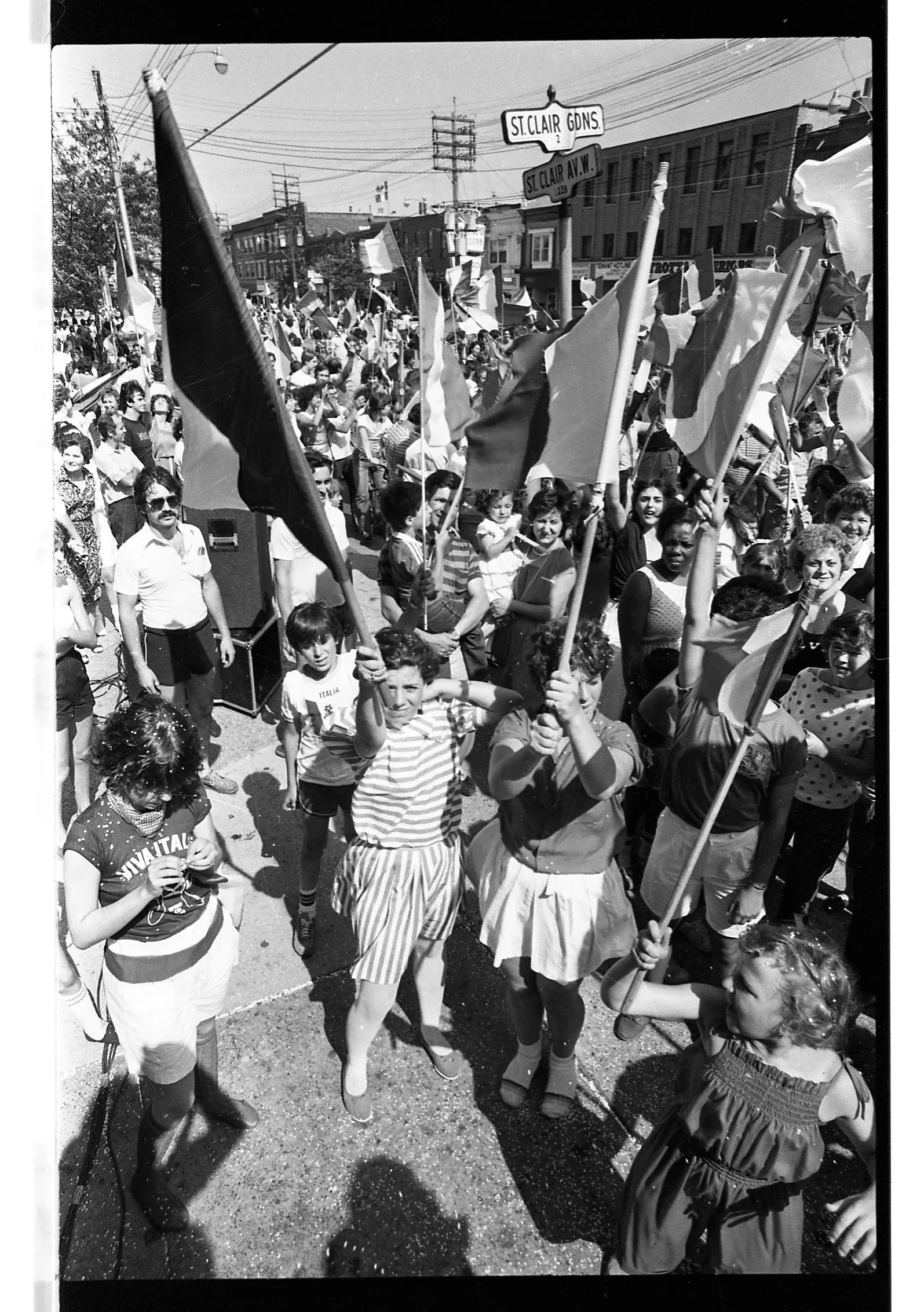 Black-and-white photo of soccer fans gathered outdoors celebrating Italy’s FIFA™ World Cup win. Fans point their flags to the sky to honour the team’s victory.