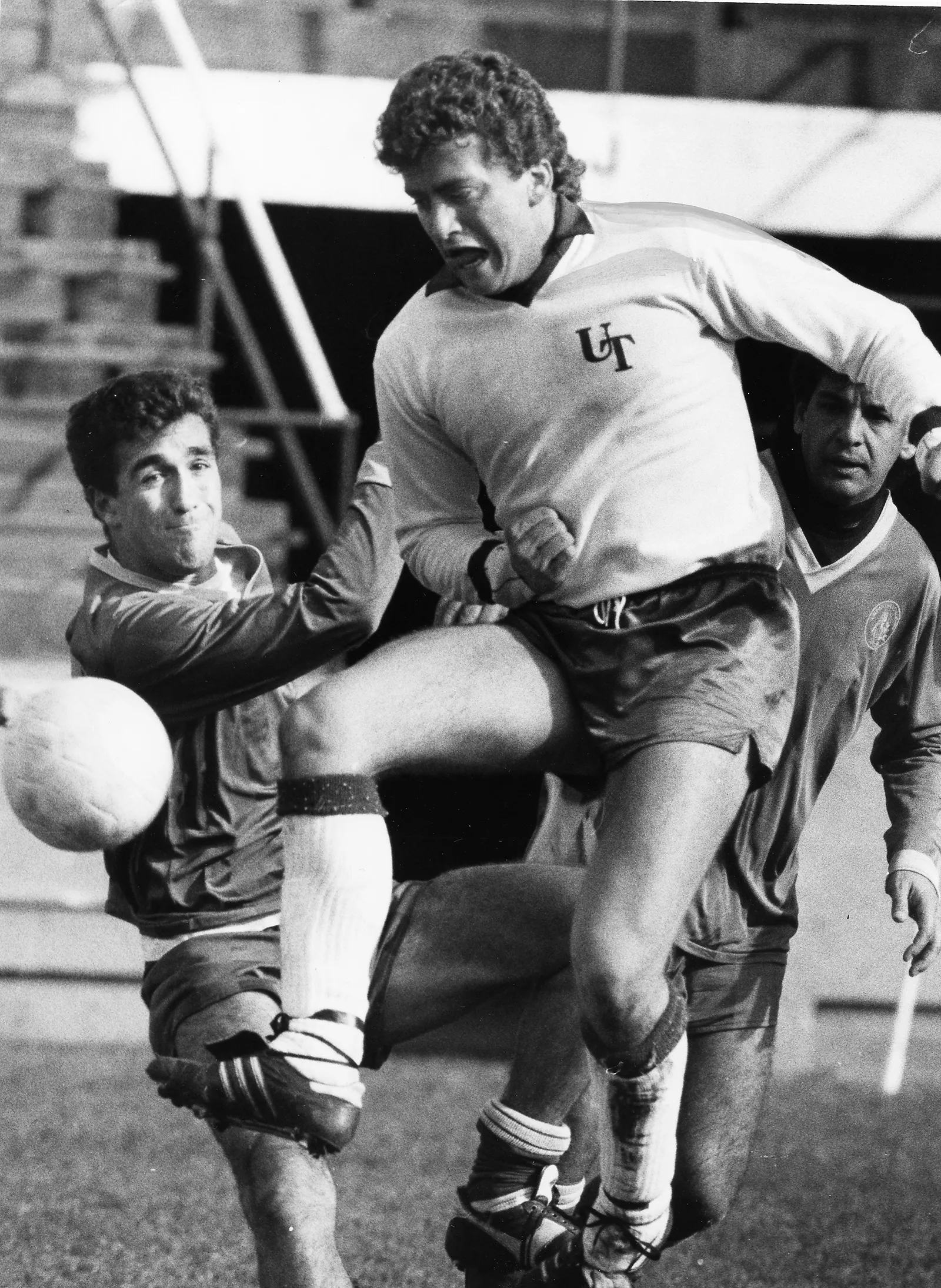 Black-and-white photo of a player on the University of Toronto team. He shields his body from two opposing players and tries to receive a pass. The tense emotions on their faces show the intensity of the game.