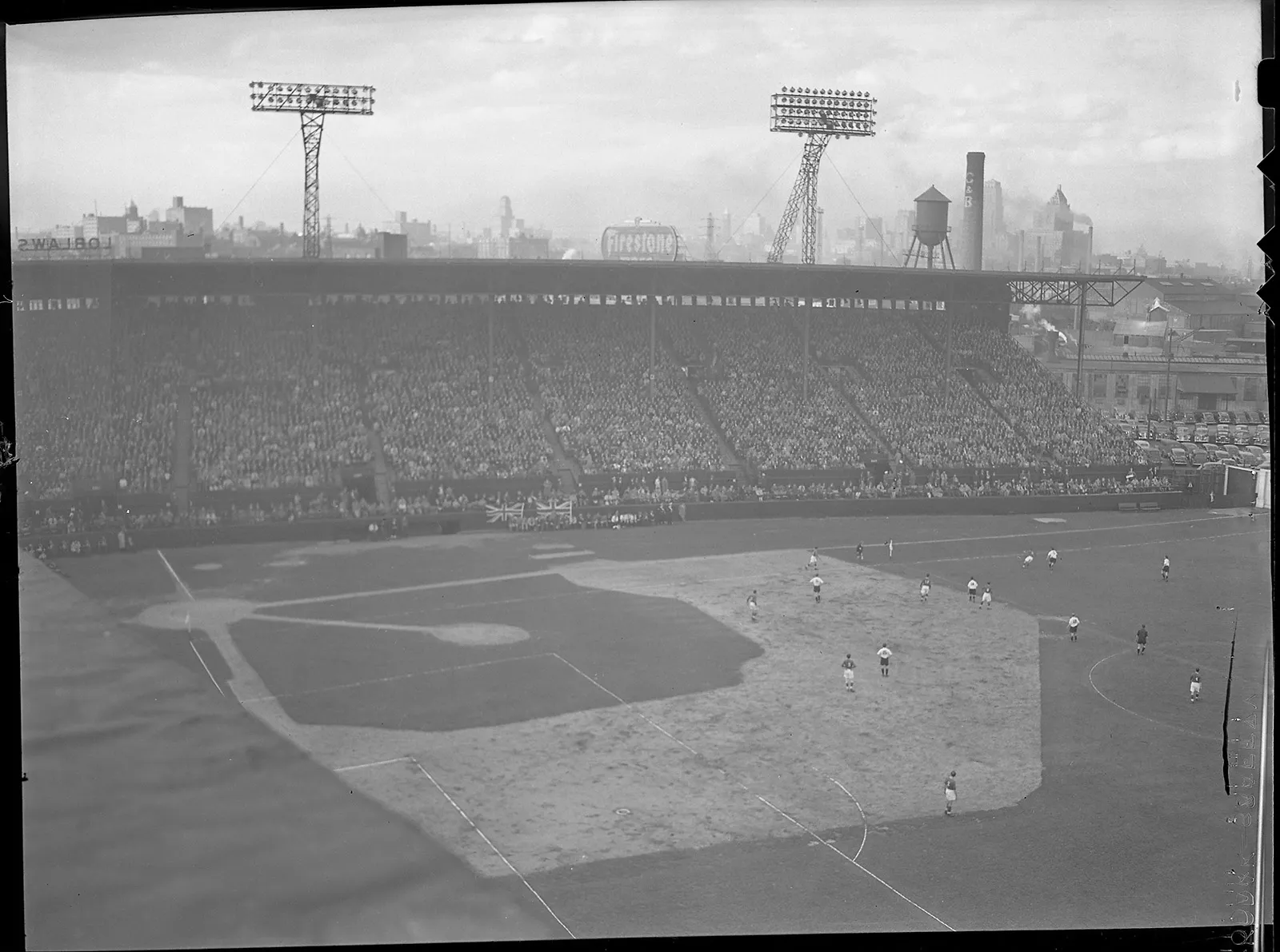 Black-and-white photo of an aerial shot of a soccer game at Maple Leaf Stadium, with the skyline of Toronto visible in the background. The soccer field is also a baseball diamond.
