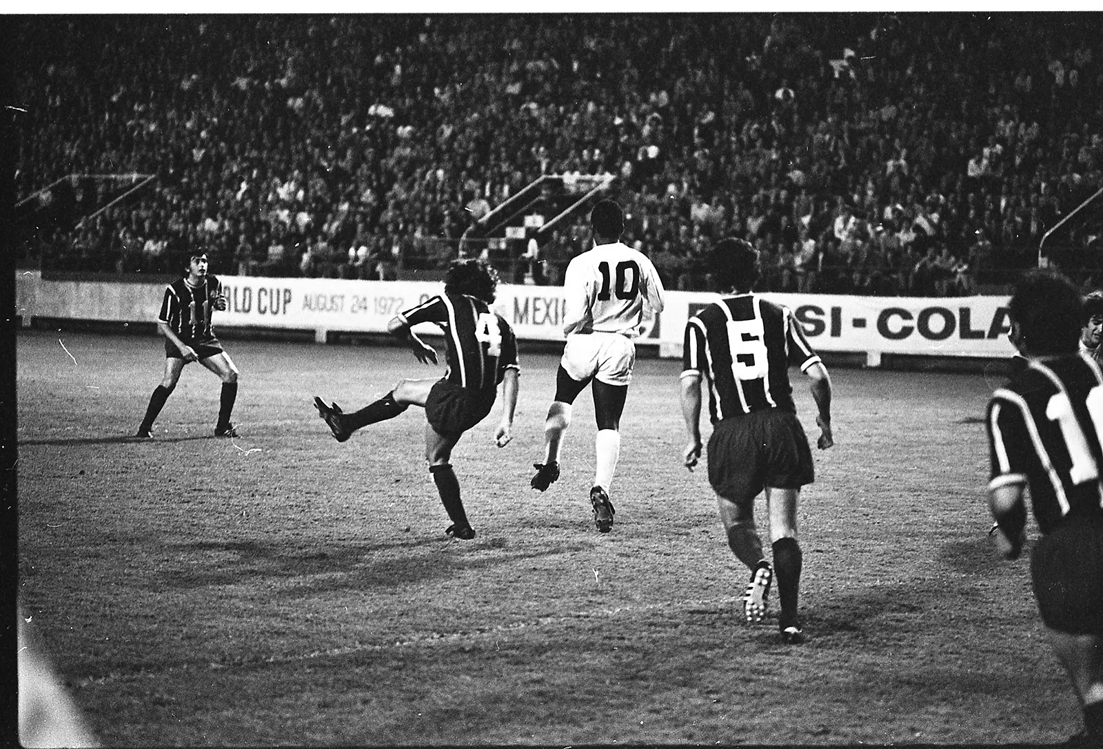 Black-and-white photo of a soccer player chesting down a ball as another player attempts to make a clearance. In the background, the stands are full of spectators.