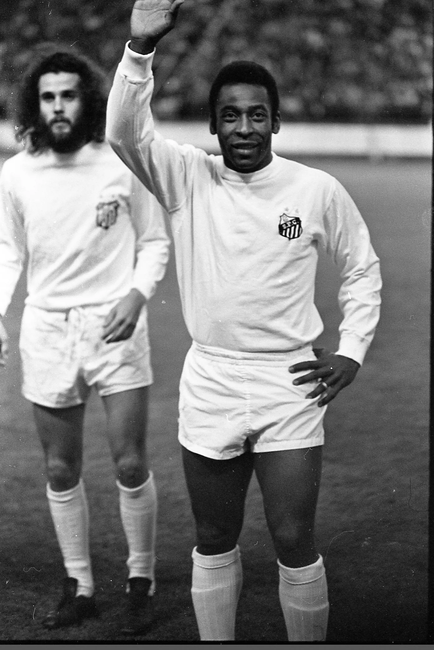 Black-and-white photo of soccer star Pelé waving to an eager crowd, ready to watch him play.