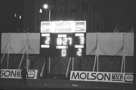 Black-and-white photo of an illuminated stadium scoreboard. The score reads 3-2 in favour of the Sting soccer team.