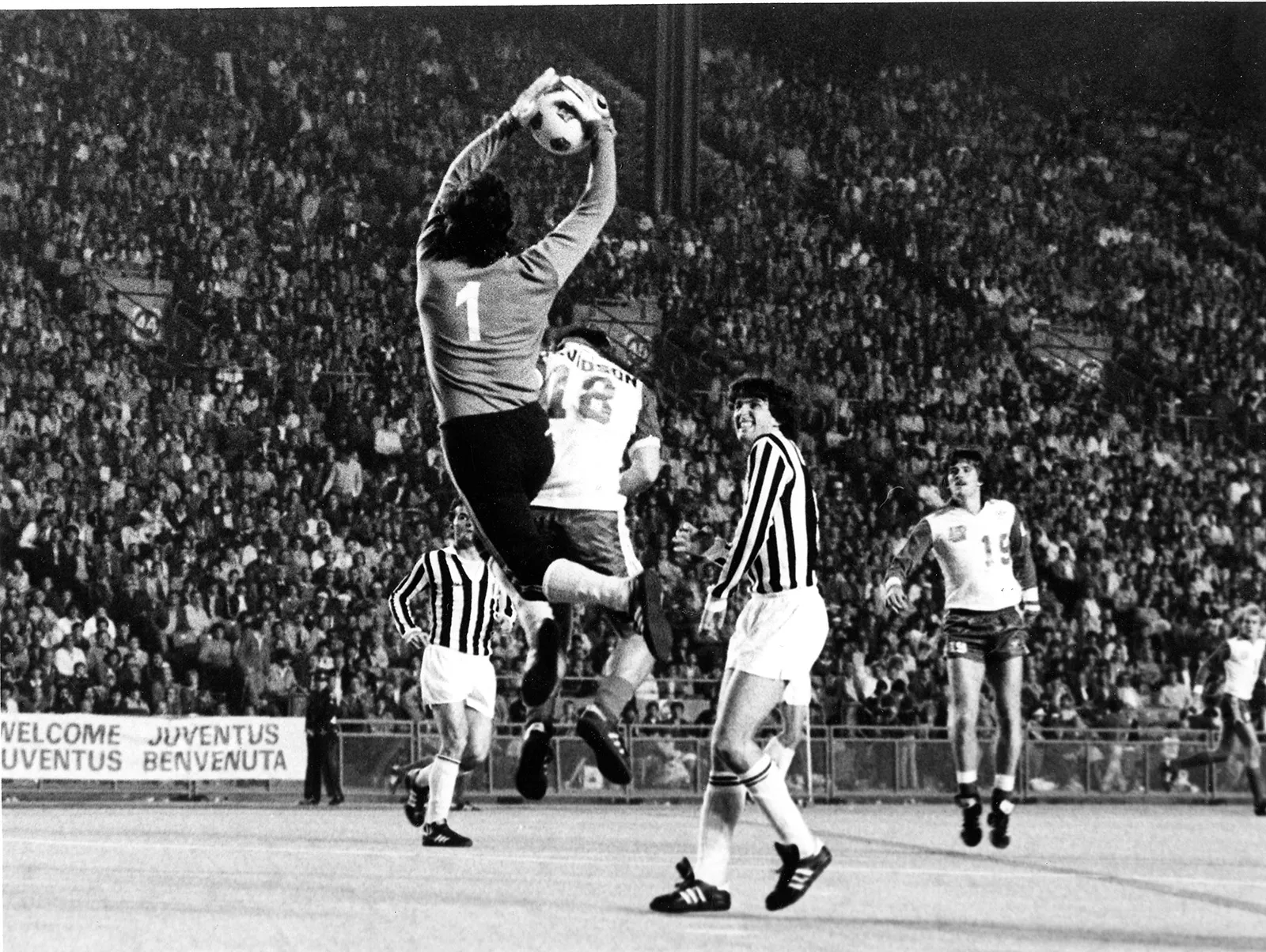 Black-and-white photo of Juventus goalie Luciano Bodini catching the ball as he jumps to grab it above the head of Toronto Blizzard’s Duncan Davidson. A huge crowd of spectators can be seen in the stands behind them.