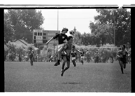 Black-and-white photo of a competitive aerial duel between two young soccer players.