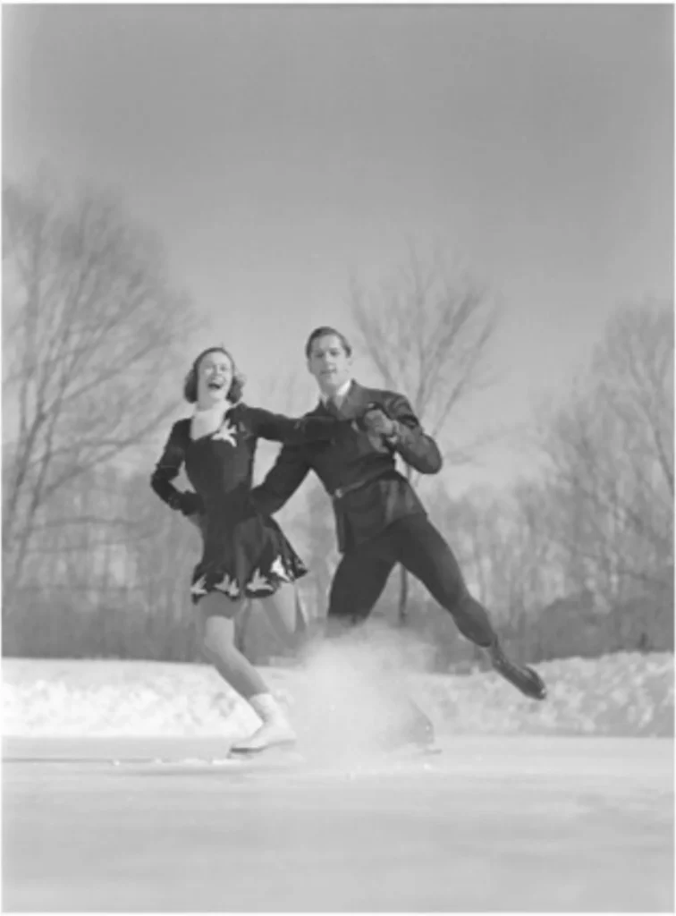 Photo en noir et blanc de deux personnes faisant du patin à glace à l’extérieur, se tenant par la main et glissant sur une surface gelée, sur fond d'arbres dénudés.