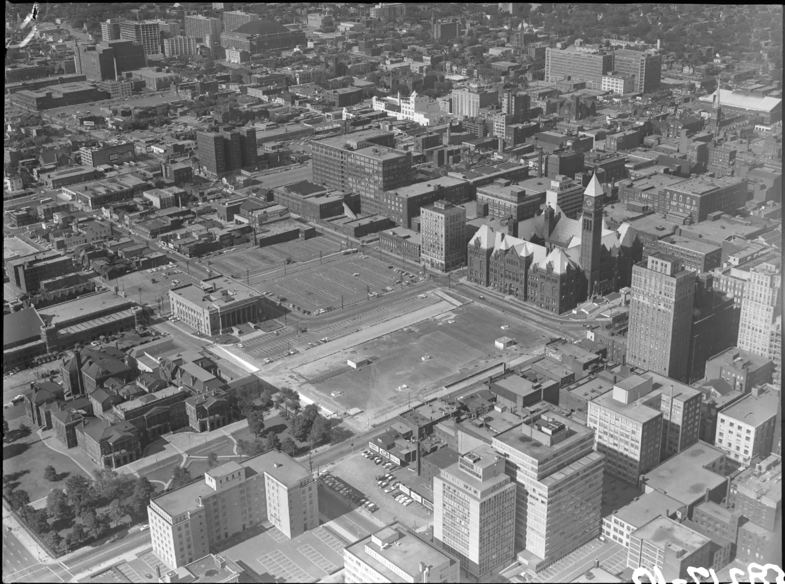 Aerial black-and-white photograph capturing Osgoode Hall and Old City Hall nestled within the dense urban landscape. A large open lot sits centrally between the two heritage buildings and the surrounding city blocks.