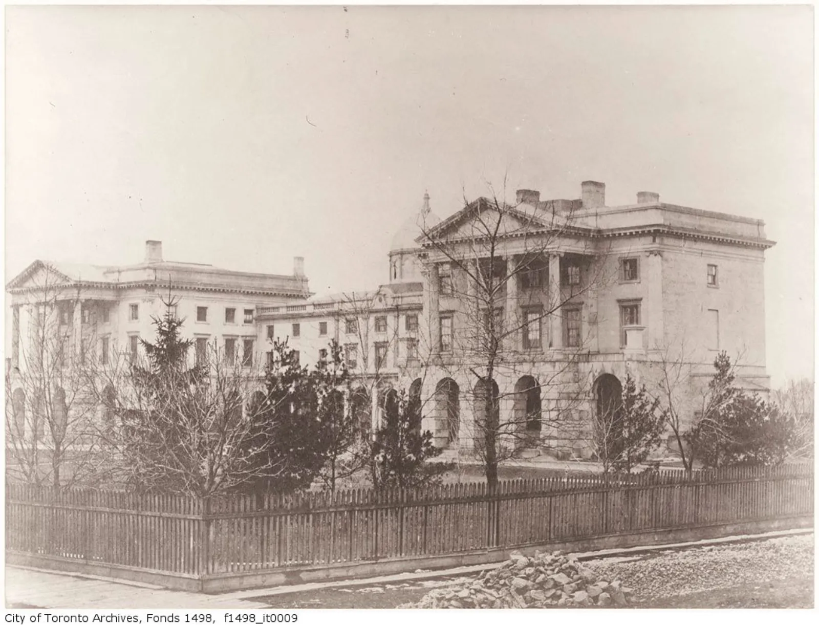 Black-and-white photograph capturing the south facade of Osgoode Hall with its central dome. A wooden fence and trees are visible in the foreground.
