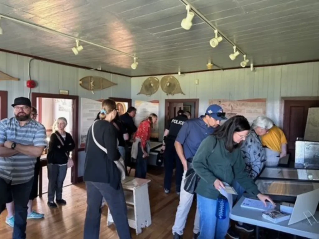 Visitors explore a heritage museum exhibit room with display tables, historical artifacts, and interpretive panels mounted on the walls.