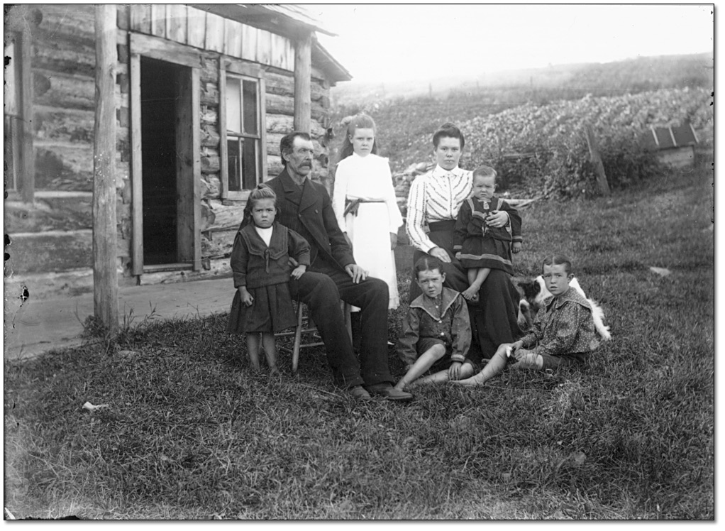 Photo: Family group outside a log building, [ca. 1900]