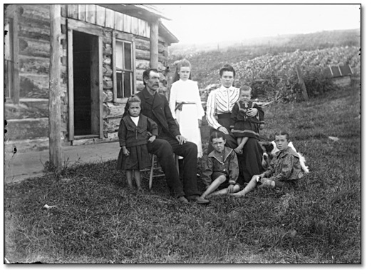 Photo: Family group outside a log building, [ca. 1900]