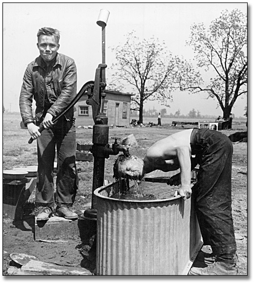 Photographie : Two men at a water pump at a farm service camp, [vers 1950] 