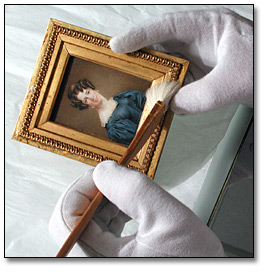 Image of framed miniature being cleaned with brush