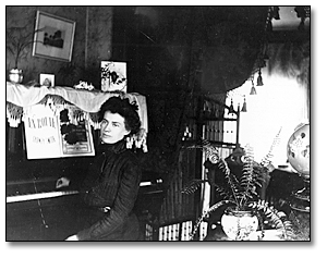 Unidentified young woman seated at a piano in a parlour, [between 1898 and 1920]