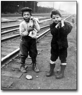 Black and white photograph of two boys near train station collecting coal from the track area