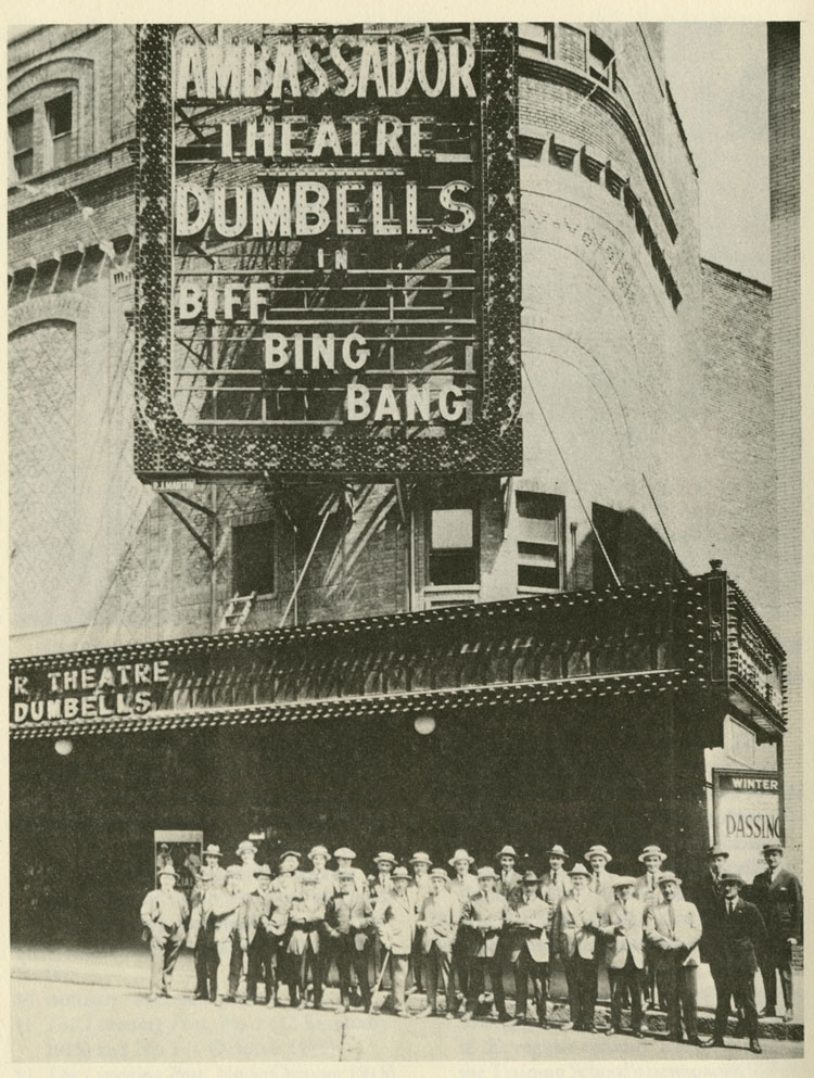 La troupe de théâtre The Dumbells à l’extérieur du théâtre Ambassador à New York, avec une marquise faisant la promotion de leur spectacle Biff, Bing, Bang