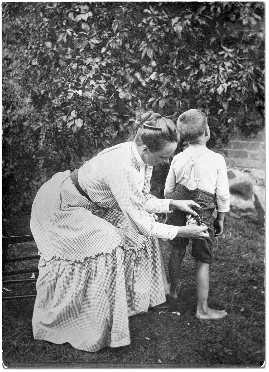 Photo: Mother sewing up little boy's pants, 1904