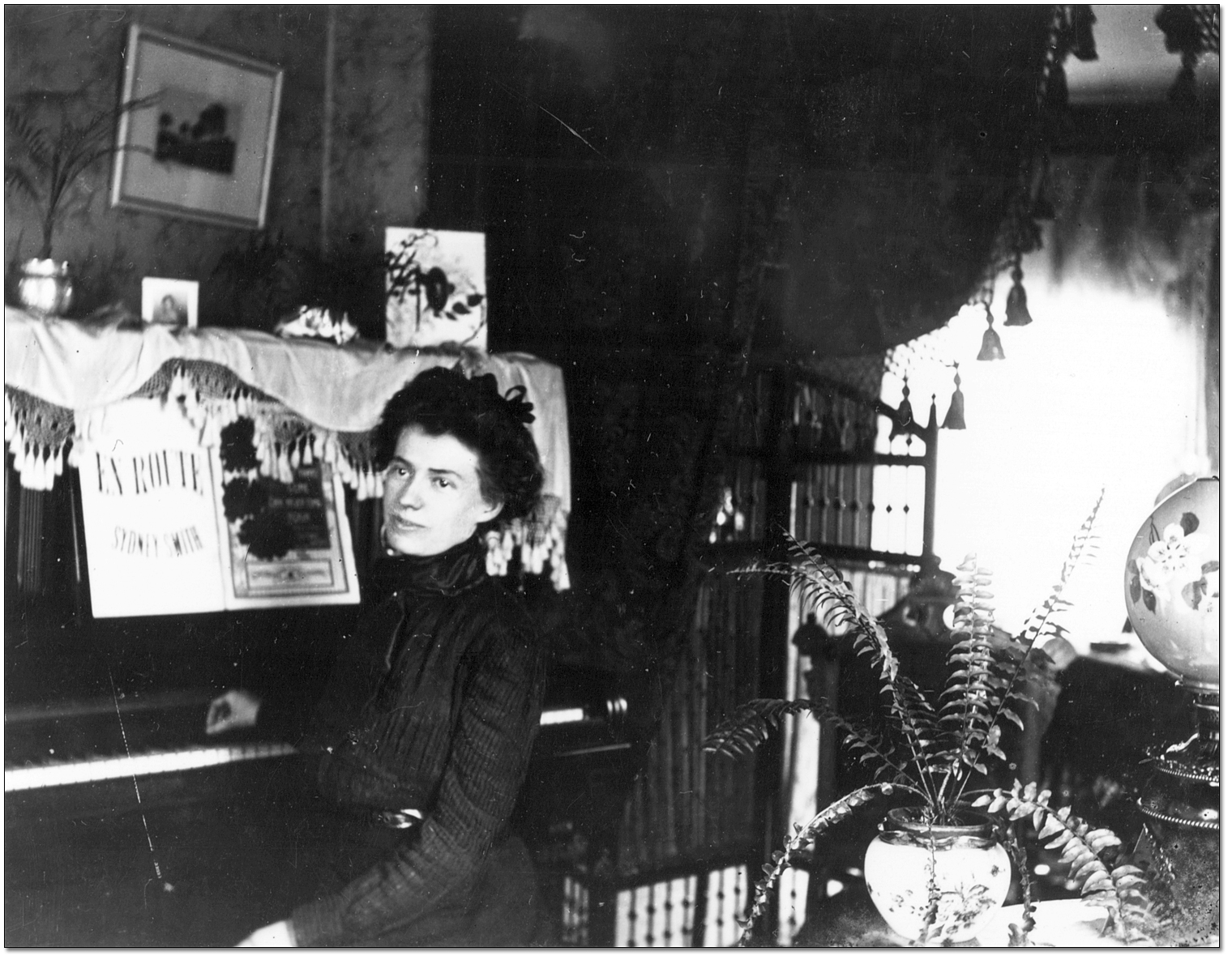Jeune femme assise devant un piano dans un salon [entre 1898 et 1920]